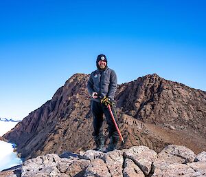 A man standing on a rocky outcrop high above the snowline.