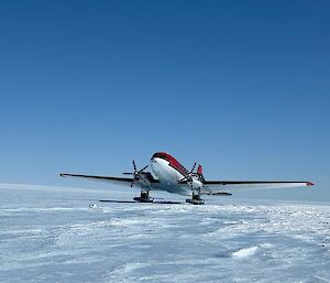 A red and white twin-engine aircraft with skis taxiing on a snow runway.
