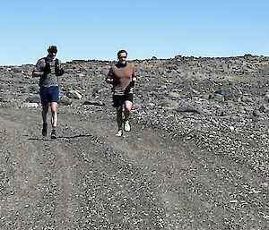 Two runners approach on a rocky road, uder a pale blue sky