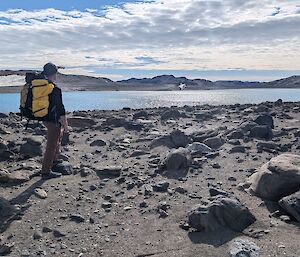 A man wearing a hiking pack admires a view over a sparkling lake.