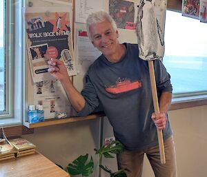 A man wearing a blue jumper points to a sign advertising walking tours of Davis, whilst holding a penguin on a stick.