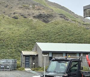 A man stands on a hill in the distance. In the foreground is a residential building and a black Polaris 4WD.