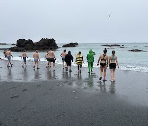 The twelve swimmers at the water's edge about to enter the ocean.
