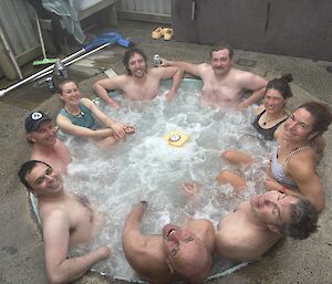 Nine people sitting around the edges of a circular spa, warming up after the ocean swim.