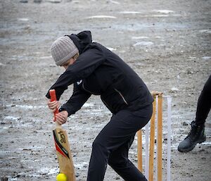 Juanita batting in front of the wickets and about to hit the ball, a fielder and road base in the background