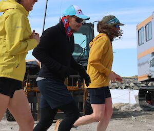 Three people running in the foreground, passing two Hagglunds parked in the background