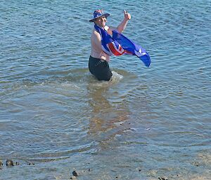 A man bathing in water, with an Australian flag draped around his shoulders and an Australian flag hat on his head.