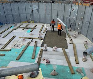 Inside a round metal structure two people are placing batts of insulation on the floor