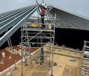 A man in high visibility clothing guides a metal purlin into place