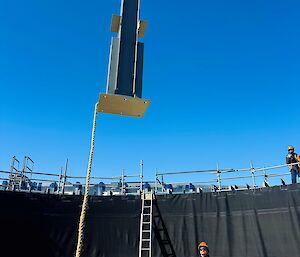 A large metal pole is lowered in from the top of frame, which is marked by a blue sky, into the circular frame of the tank.