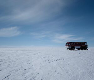 A red and white terrabus parked on a flat expanse of white ice.