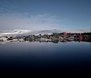 Mawson station reflected in the calm blue water of the bay.