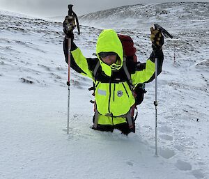 A man wearing outdoor clothing and carrying a backpack stands in thigh-deep snow.