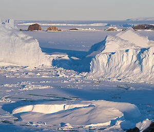 Two large icebergs sit in a frozen sea area.