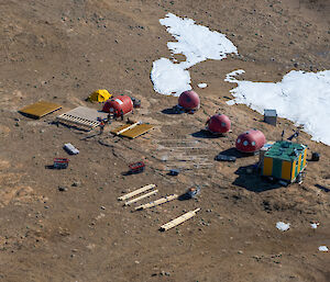 Four red domes, a green and yellow striped but and a bright yellow test sit in a rocky landscape where a wooden deck is under construction, with construction material around the area
