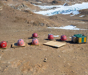 A scene looking dwn from above into a brown rocky landscape with six red domes, a green and yellow striped hut and a large wooden platform clustered together.