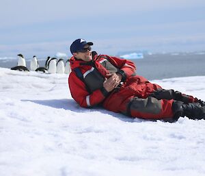 Stewart is laying on the ice with several penguins behind him