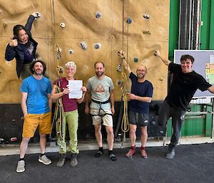 A group of 6 people stand proudly in front of a climbing wall