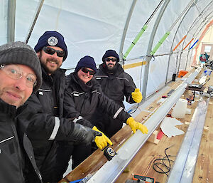 Four people pointing to an ice core on a v-shaped tray, set up on a wooden bench.