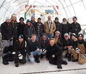 A group of 18 people arranged for a photo inside the drilling tent. About half are standing and the other half kneeling in front.