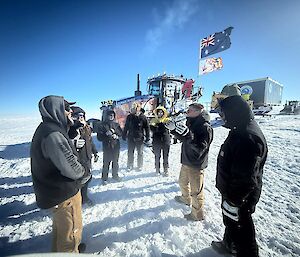 A group of people standing in a circle talking, with a tractor flying the Australian flag behind.
