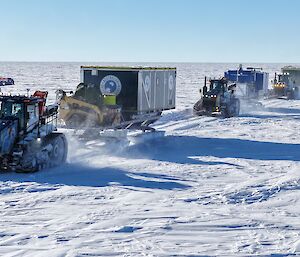 Three tractors in a line, each towing sleds carring shipping containers and other equipment.