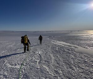 Two expeditioners walking across the flat white ice.
