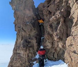 A group of expeditioners climbing a steep exposed mountain in Antarctica.