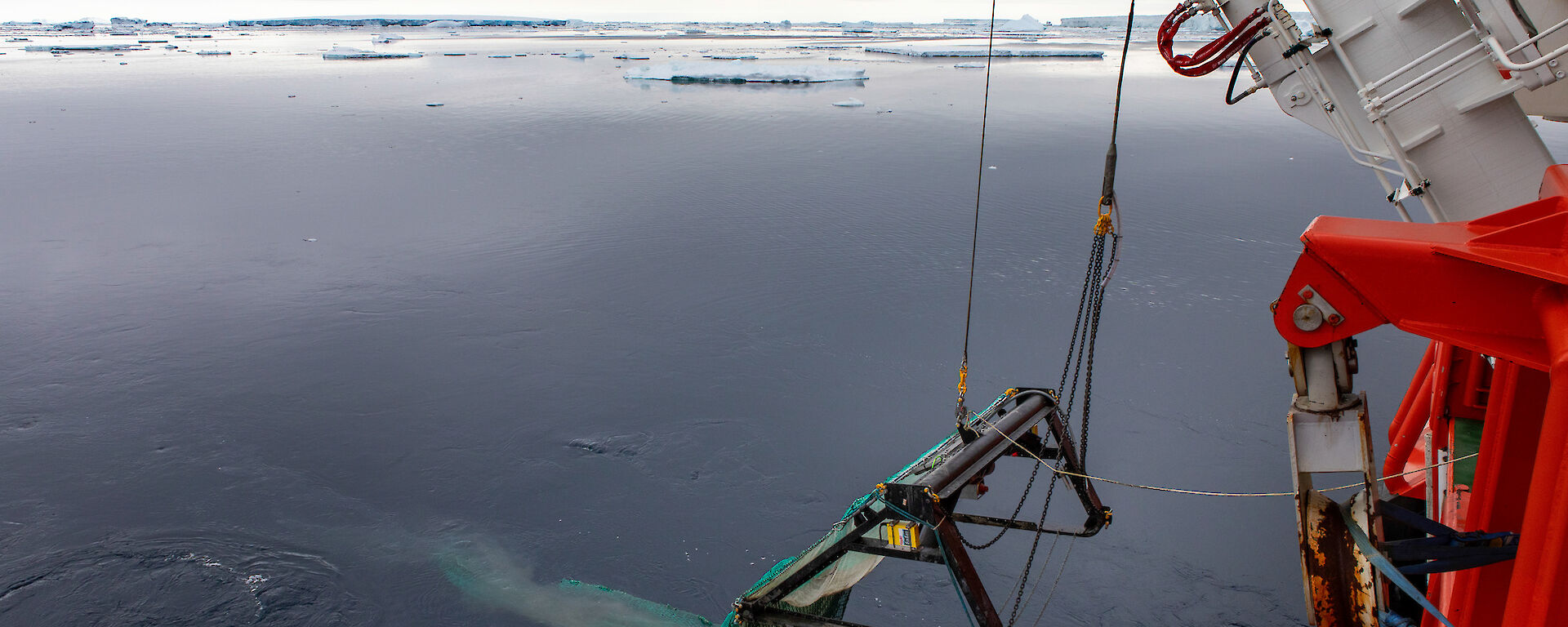 A beam trawl being lowered into the water from RSV Nuyina by a crane