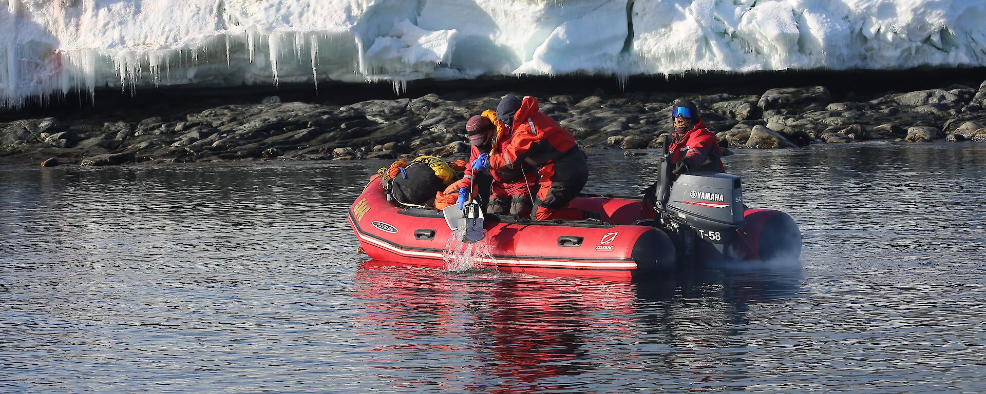 Three people are pictured in the red IRB in the foreground, two people taking samples and one driver at the tiller. The Wilkes shoreline in the background