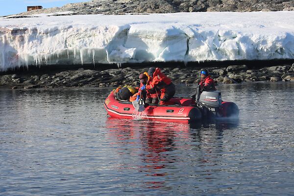Three people are pictured in the red IRB in the foreground, two people taking samples and one driver at the tiller. The Wilkes shoreline in the background