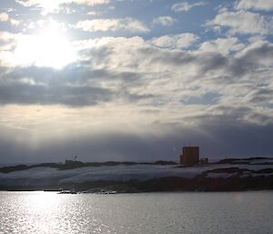 The sun protruding from a cloud, over a landscape view of old Wilkes station, taken from the water