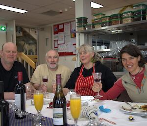 Four people sitting at a table, set with bottles of wine and glasses or orange juice.