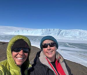A selfie of two women with an ice cliff behind.