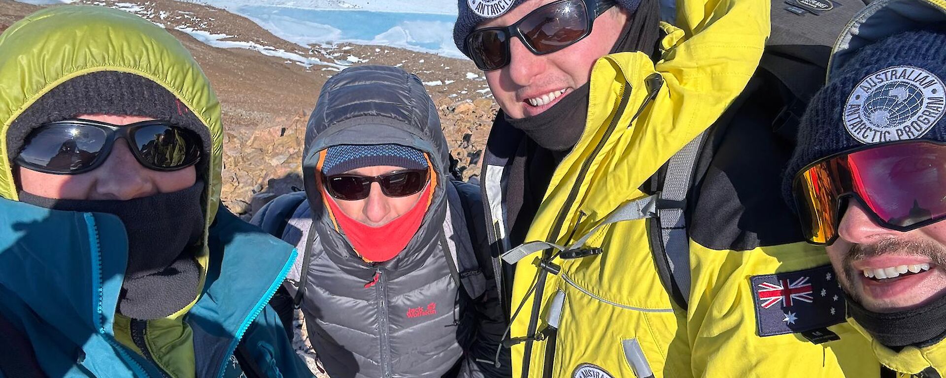 A selfie of four people rugged up against the cold on top of a rocky mountain peak.