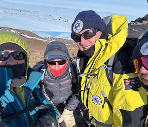 A selfie of four people rugged up against the cold on top of a rocky mountain peak.