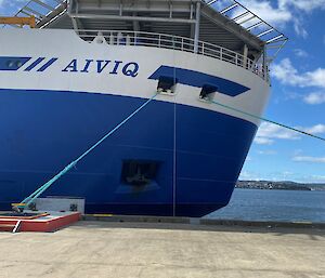 The bow of a blue and white ship, anchored to a concrete wharf.