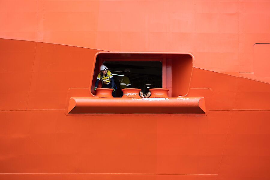 A close up of an open portal in the side of a red ship with a lady in hi-vis popping her head out