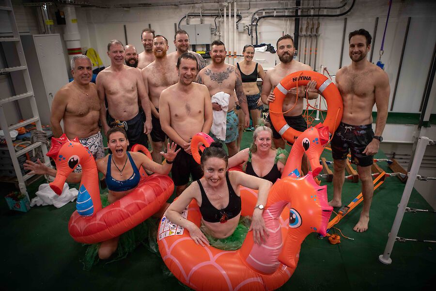 A group of people in bathers, some wearing blow-up sea horse life buoys