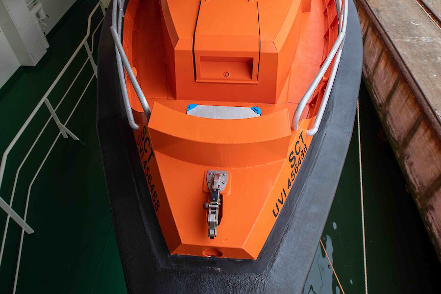 An smaller orange boat attached to the side of a ship